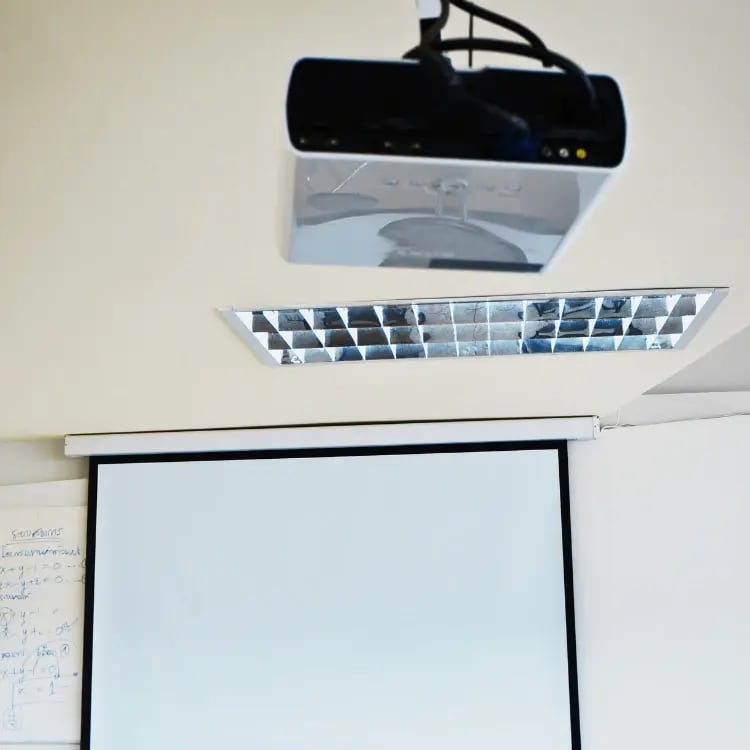 Ceiling-mounted classroom projector with pull-down screen, ready for use in a school learning space
