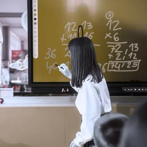 Teacher writing a maths equations on an interactive classroom panel during a lesson.
